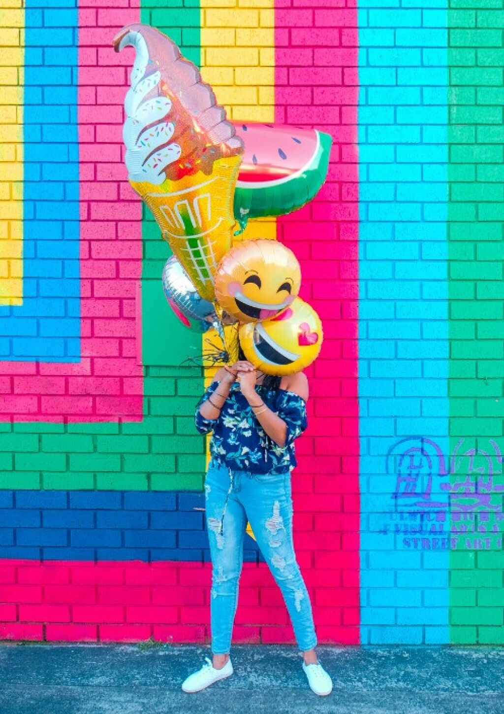 Frau vor bunter Wand mit Emoji Luftballons